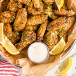 Pinterest graphic for Lemon Pepper Wings. Image shows overhead of basket of Lemon Pepper Wings with lemon wedges and small cup of dipping sauce. Says "super easy Lemon Pepper Wings simplejoy.com"