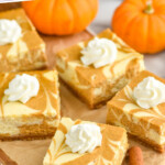 Pinterest graphic for Pumpkin Cheesecake Bars. Text says "Pumpkin Cheesecake Bars simplejoy.com" Image shows cut Pumpkin Cheesecake Bars topped with whipped cream. Small pumpkins and two cinnamon sticks sitting beside