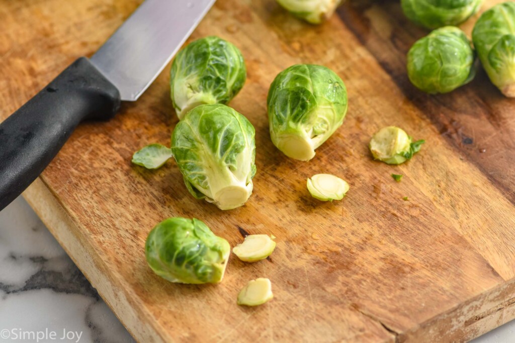 brussel sprouts with stems cut off sitting on a wooden cutting board with a chef's knife sitting beside