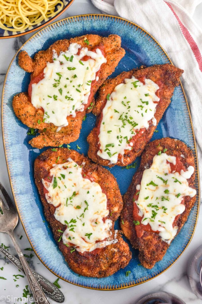 plate of four pieces of Chicken Parmesan topped with melted cheese and fresh parsley