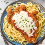 plate of spaghetti noodles topped with Chicken Parmesan, melted cheese, and fresh parsley. Fork and glass of red wine sitting beside