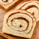 slices of cinnamon bread on a wooden cutting board with cinnamon sticks sitting beside