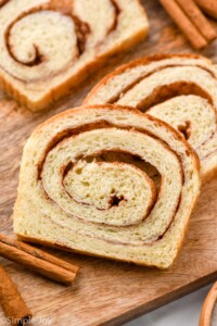 slices of cinnamon bread on a wooden cutting board with cinnamon sticks sitting beside