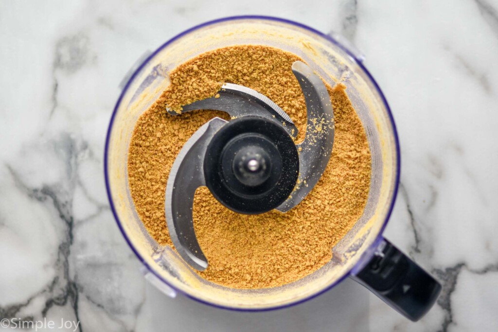 overhead of food processor of graham cracker crust ingredients to make Pumpkin Cheesecake Bars