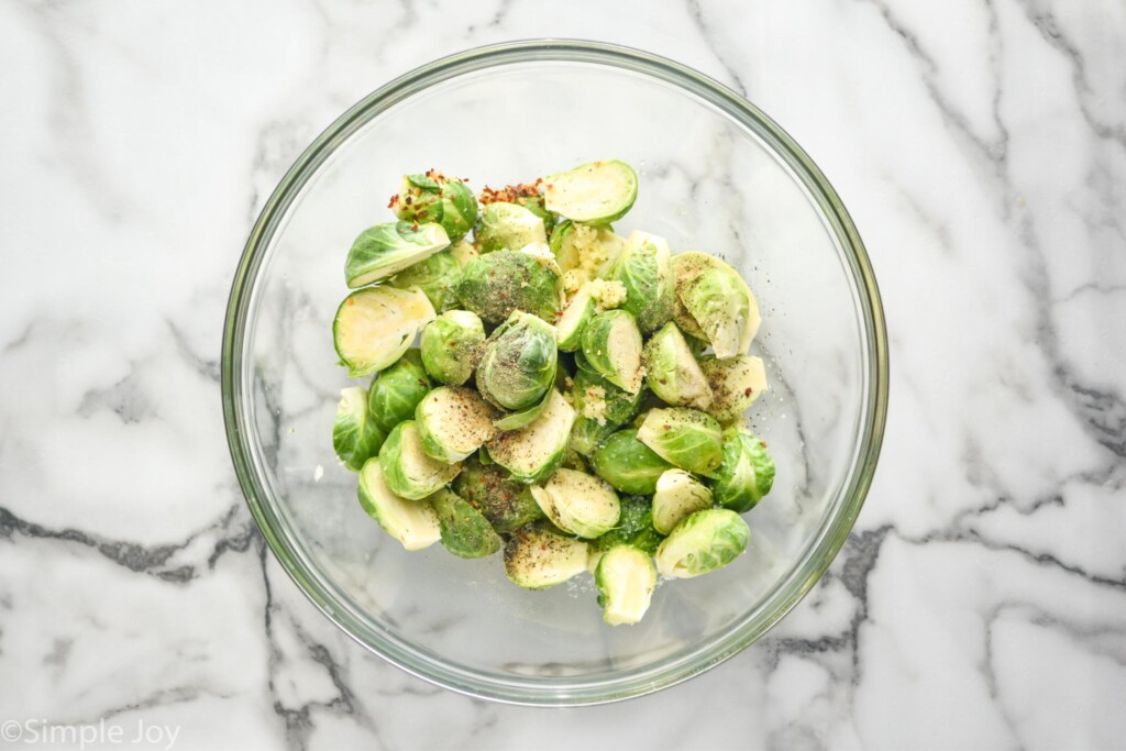 overhead of large glass bowl of halved brussels sprouts and seasonings to make Air Fryer Brussels Sprouts