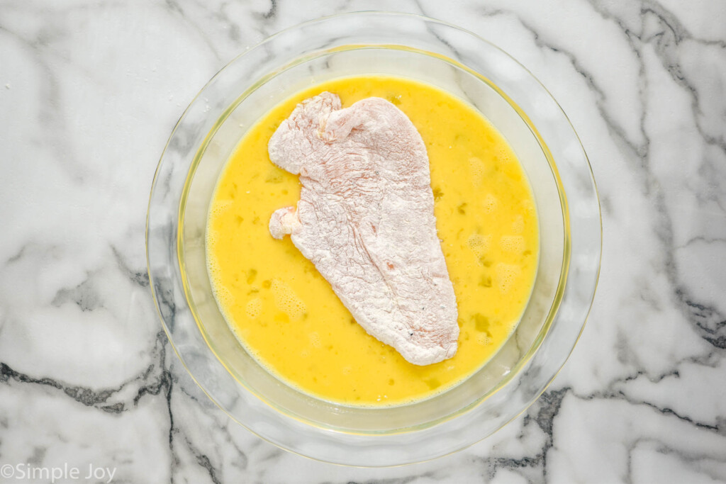 overhead of chicken cutlet covered in flour sitting in a bowl of beaten eggs to make Chicken Parmesan