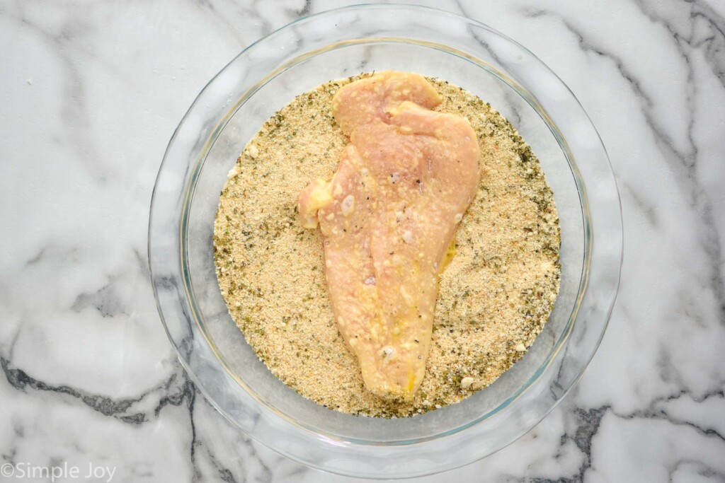 overhead of glass bowl of seasonings and breadcrumbs with a chicken cutlet sitting on top to make Chicken Parmesan