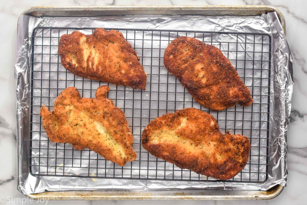 overhead of cooked chicken cutlets on a wire rack over a foil lined baking sheet to make Chicken Parmesan