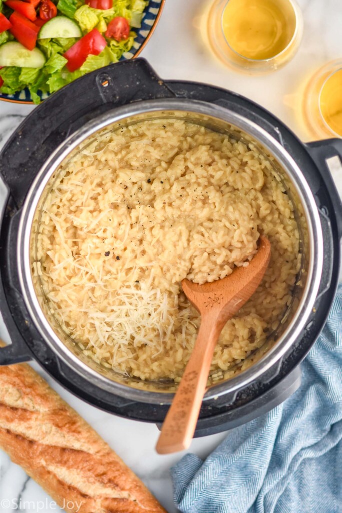 overhead of instant pot of risotto topped with parmesan cheese and wooden spoon inside