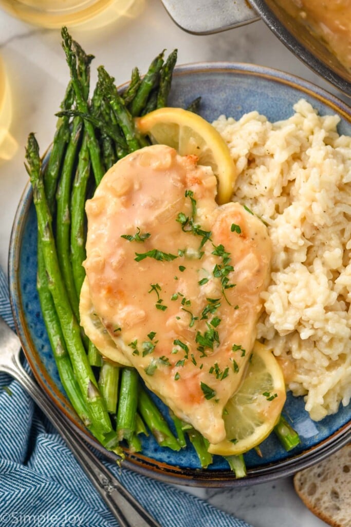 Plate of asparagus, risotto, and Lemon Chicken topped with fresh parsley, two lemon slices sitting beside