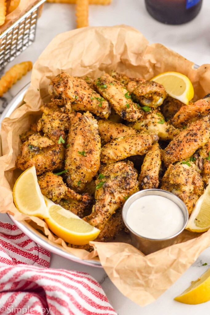 Basket of Lemon Pepper Wings with lemon wedges and a small cup of white dipping sauce