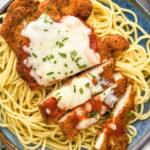 Plate of spaghetti noodles topped with Chicken Parmesan, melted cheese, and fresh parsley