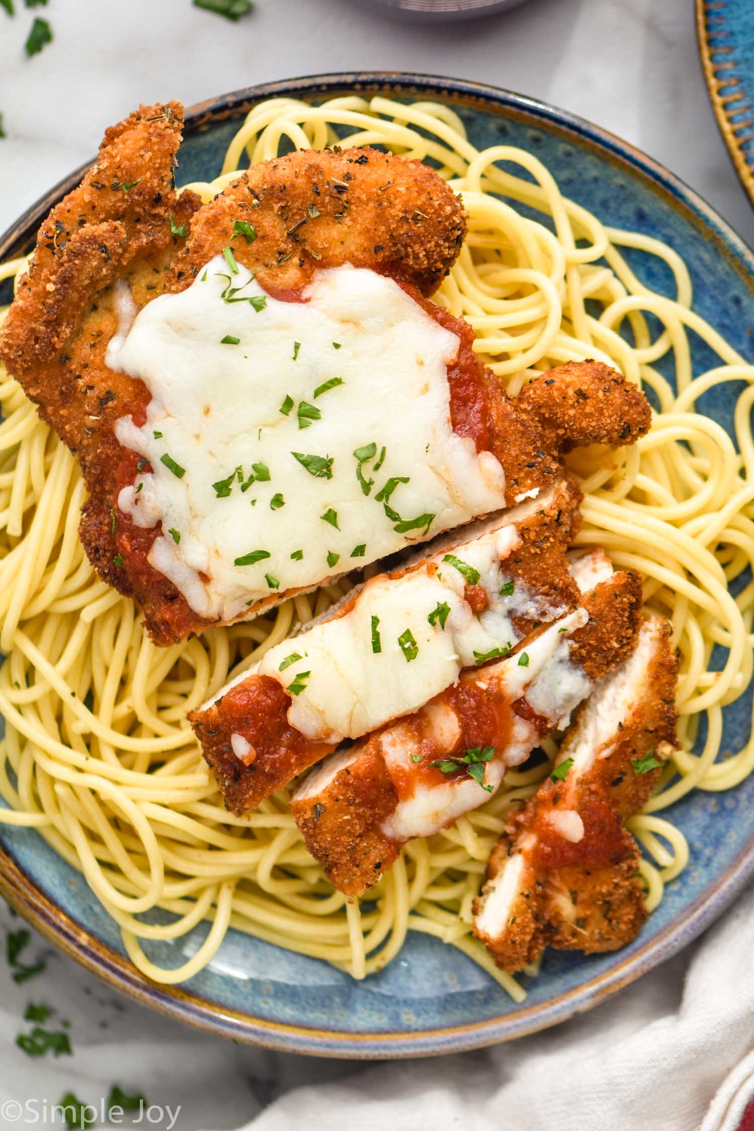 Plate of spaghetti noodles topped with Chicken Parmesan, melted cheese, and fresh parsley