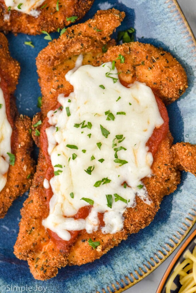 Close up of Chicken Parmesan on a plate topped with melted cheese and fresh parsley