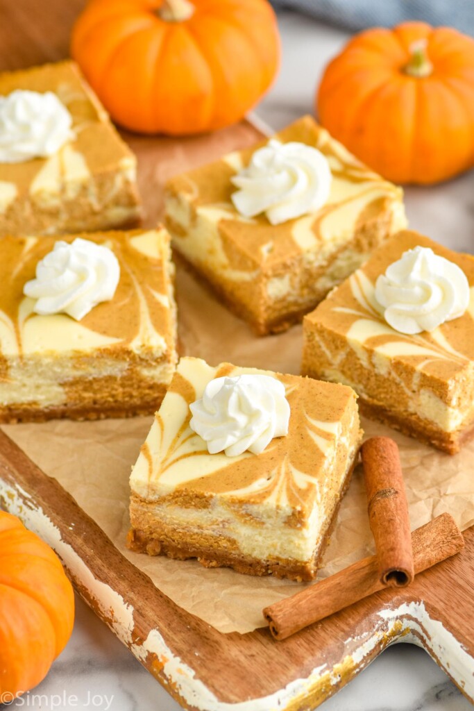 Pumpkin Cheesecake Bars topped with a dollop of whipped cream. Pumpkins and cinnamon sticks sitting beside