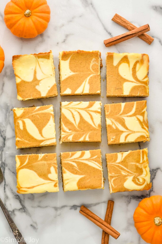 overhead of Pumpkin Cheesecake Bars with cinnamon sticks and small pumpkins sitting beside