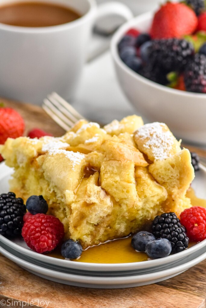 piece of crockpot french toast topped with maple syrup and powdered sugar with fresh berries beside