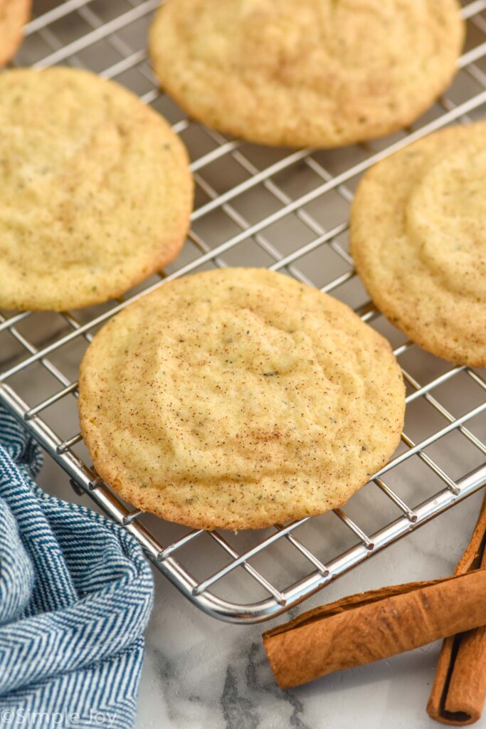 Chai Sugar Cookies sitting on a wire cooling rack with two cinnamon sticks sitting in front of rack