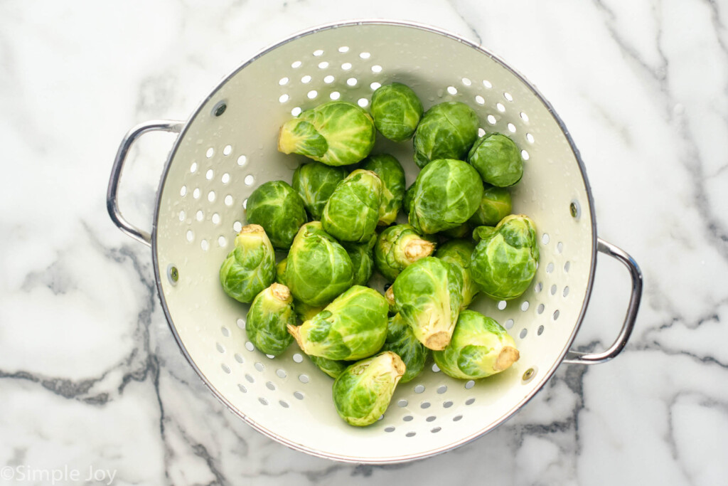 overhead of a white colander of washed raw brussel sprouts