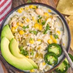 overhead of bowl of Crockpot White Chicken Chili with a spoon topped with avocado slices, jalapeño slices, and fresh cilantro.