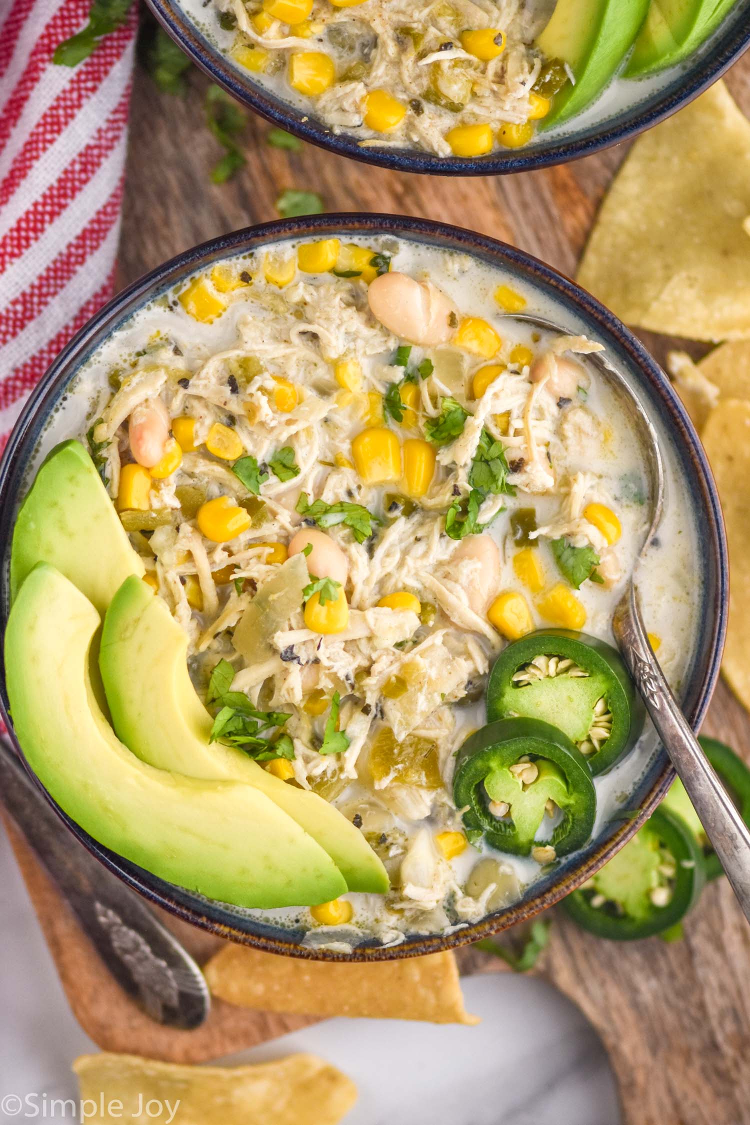 overhead of bowl of Crockpot White Chicken Chili with a spoon topped with avocado slices, jalapeño slices, and fresh cilantro.