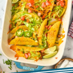 Pinterest graphic for baked tacos. Image shows overhead of casserole dish of baked tacos topped with shredded lettuce, diced tomatoes, lime wedges, and Jalapeños. Says "baked tacos simplejoy.com"