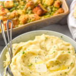 Pinterest graphic for crockpot mashed potatoes. Text says "slow cooker mashed potatoes simplejoy.com" Image shows a bowl of crockpot mashed potatoes topped with fresh parsley and butter with two spoons for serving. Casserole dish of brussels sprouts casserole sitting in background