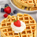 Pinterest graphic for Waffle Recipe. Text says "the best Waffle Recipe simplejoy.com" Image shows waffles on a plate topped with whipped cream and a strawberry with fresh berries and another plate of waffles sitting behind.