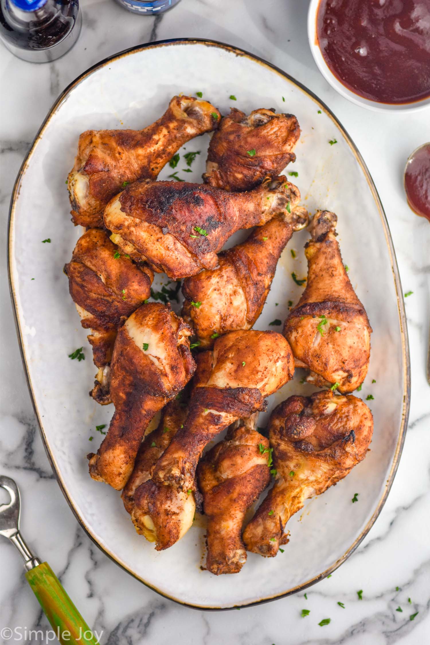 overhead of platter of Oven Baked Chicken Legs with bowl of bbq sauce sitting beside