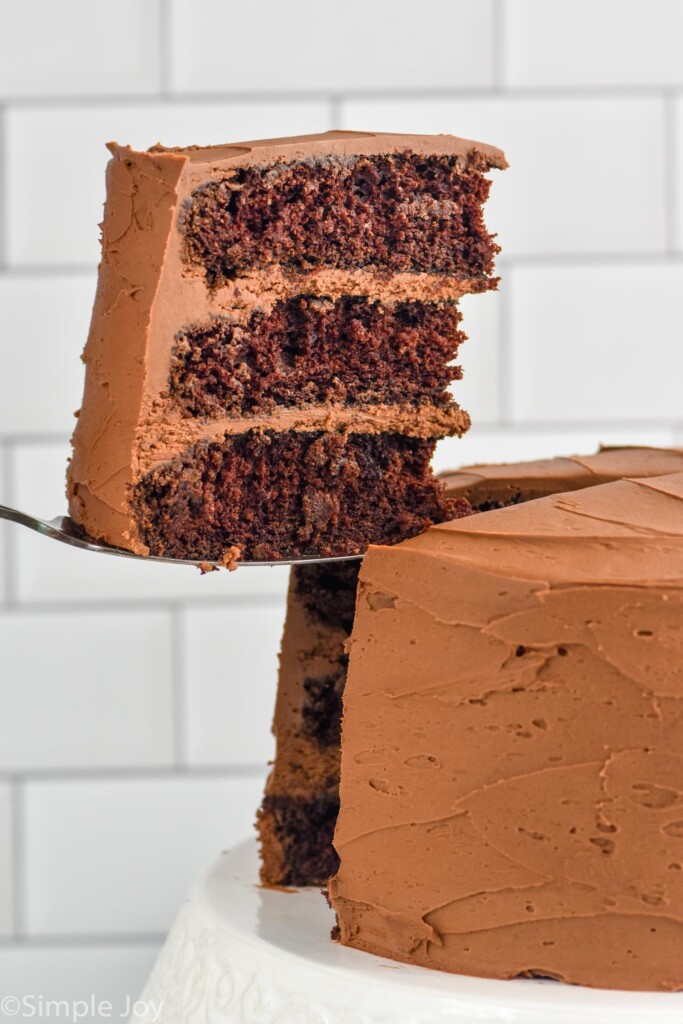 Spatula holding piece of layered chocolate cake out of frosted chocolate cake on a cake stand