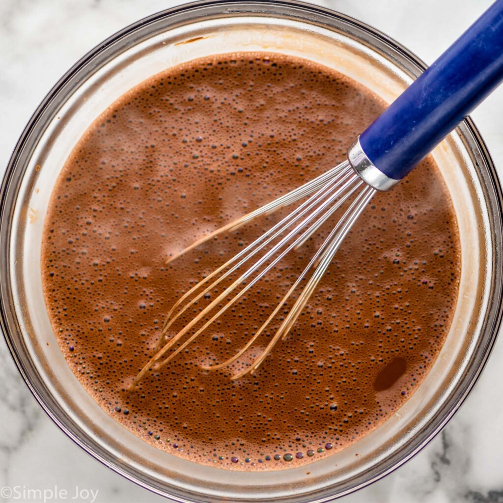 overhead of glass bowl of cocoa powder and hot water to make chocolate cake. Wire whisk sitting in bowl