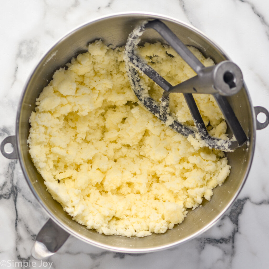 overhead of metal mixing bowl with creamed butter and sugar and paddle attachment to make chocolate cake