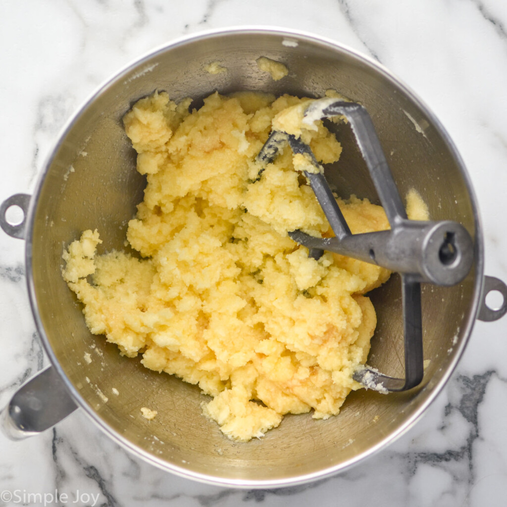 overhead of metal mixing bowl with creamed butter and sugar, eggs, vanilla, and paddle attachment to make chocolate cake