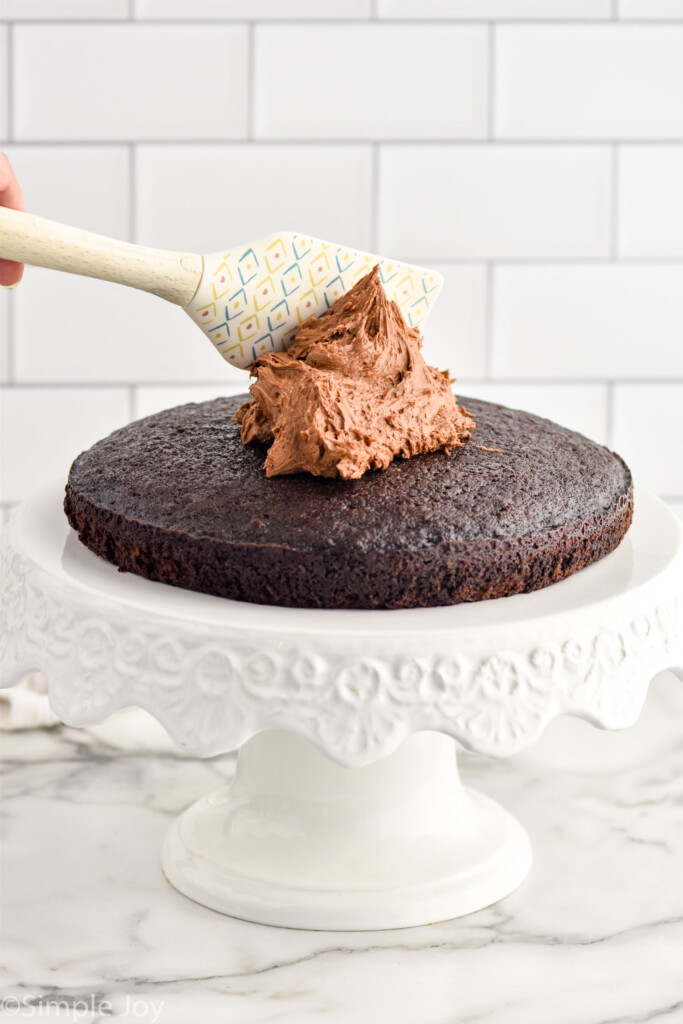 Single layer of Chocolate Cake sitting on a cake stand with dollop of chocolate frosting and spatula on top