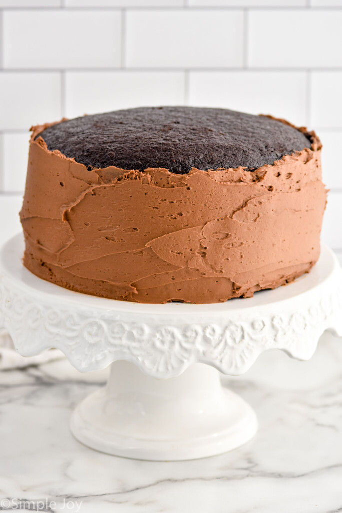 Chocolate Cake sitting on a cake stand with chocolate frosting on the sides of the cake