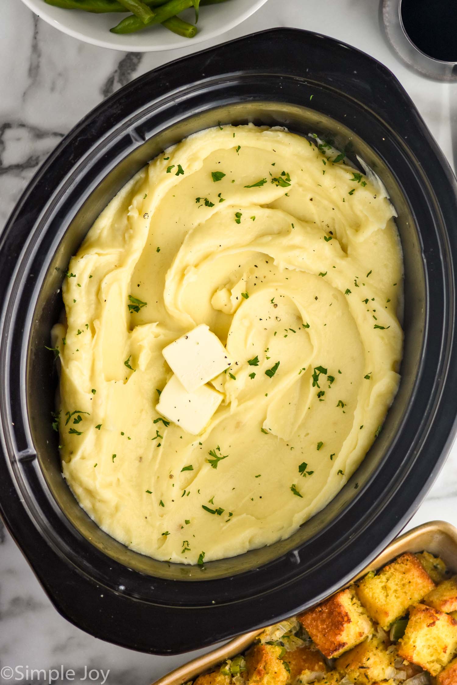 overhead of crockpot of crockpot mashed potatoes mashed potatoes topped with butter and fresh parsley