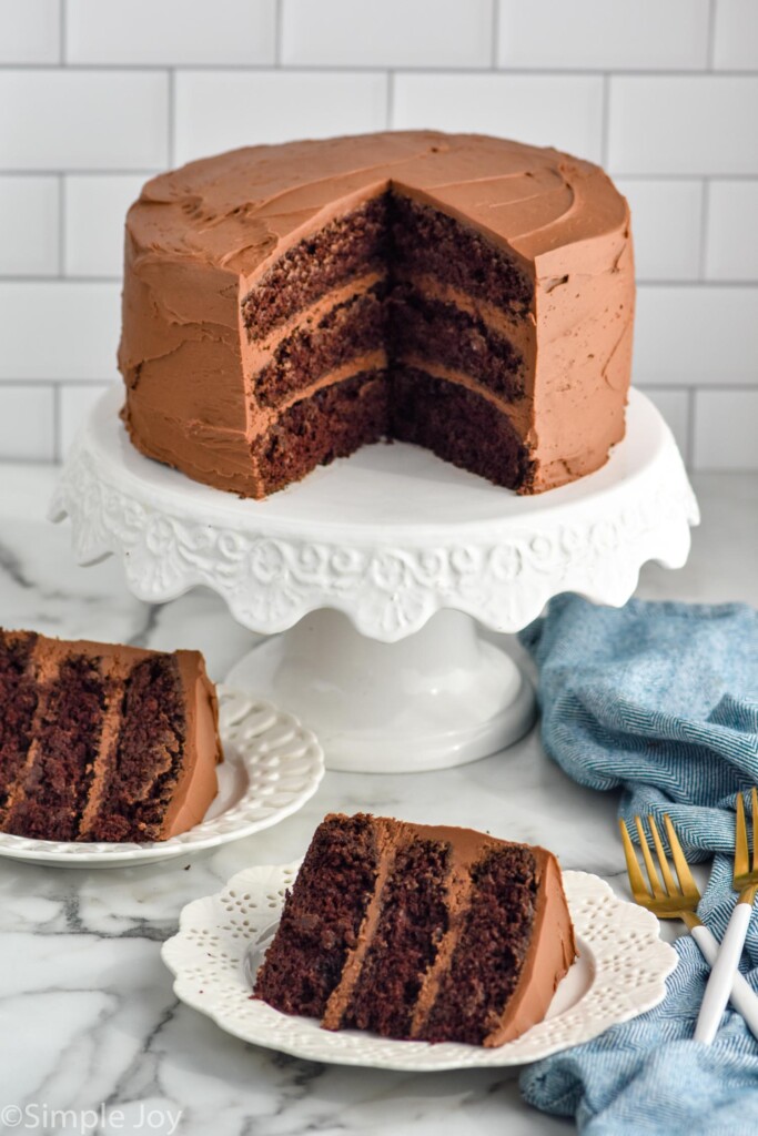 homemade Chocolate Cake on a cake stand with two pieces of layered Chocolate Cake on plates and two forks sitting in front