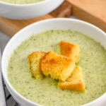 bowl of Cream of Broccoli Soup topped with croutons, bowl of Cream of Broccoli Soup and croutons sitting in background