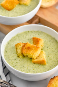 bowl of Cream of Broccoli Soup topped with croutons, bowl of Cream of Broccoli Soup and croutons sitting in background