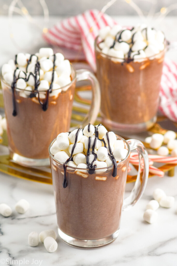 Three mugs of homemade Hot Chocolate topped with marshmallows and chocolate sauce drizzle