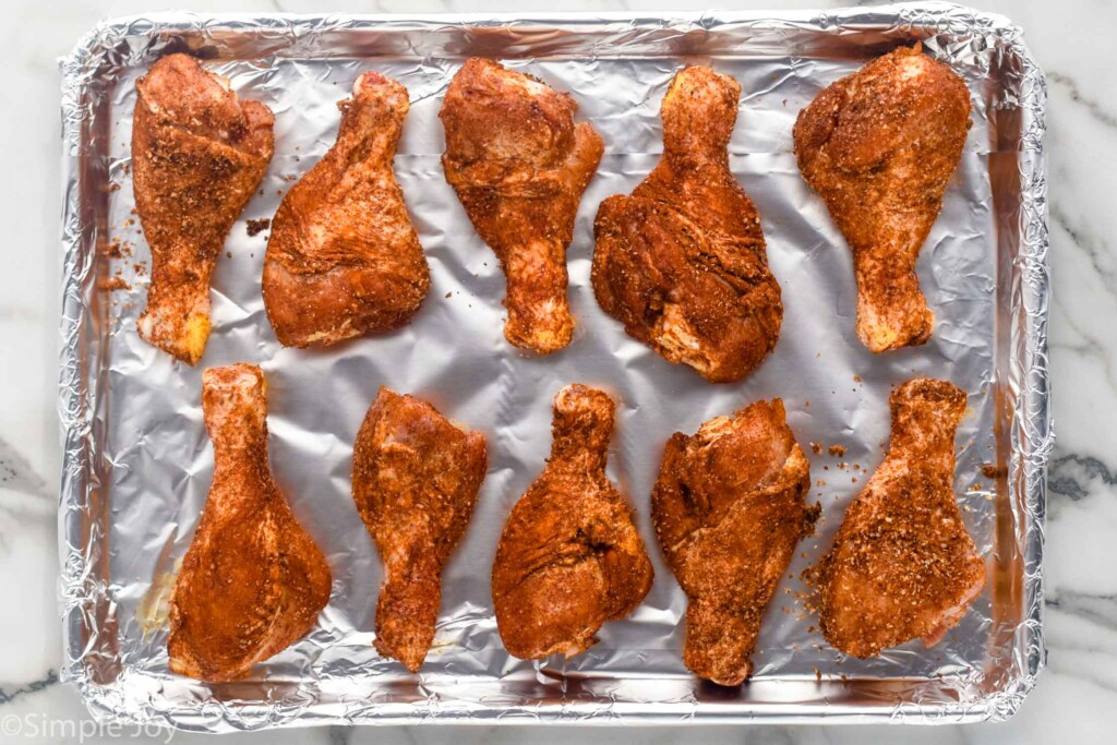 overhead of foil lined baking sheet with seasoning chicken legs to make Oven Baked Chicken Legs