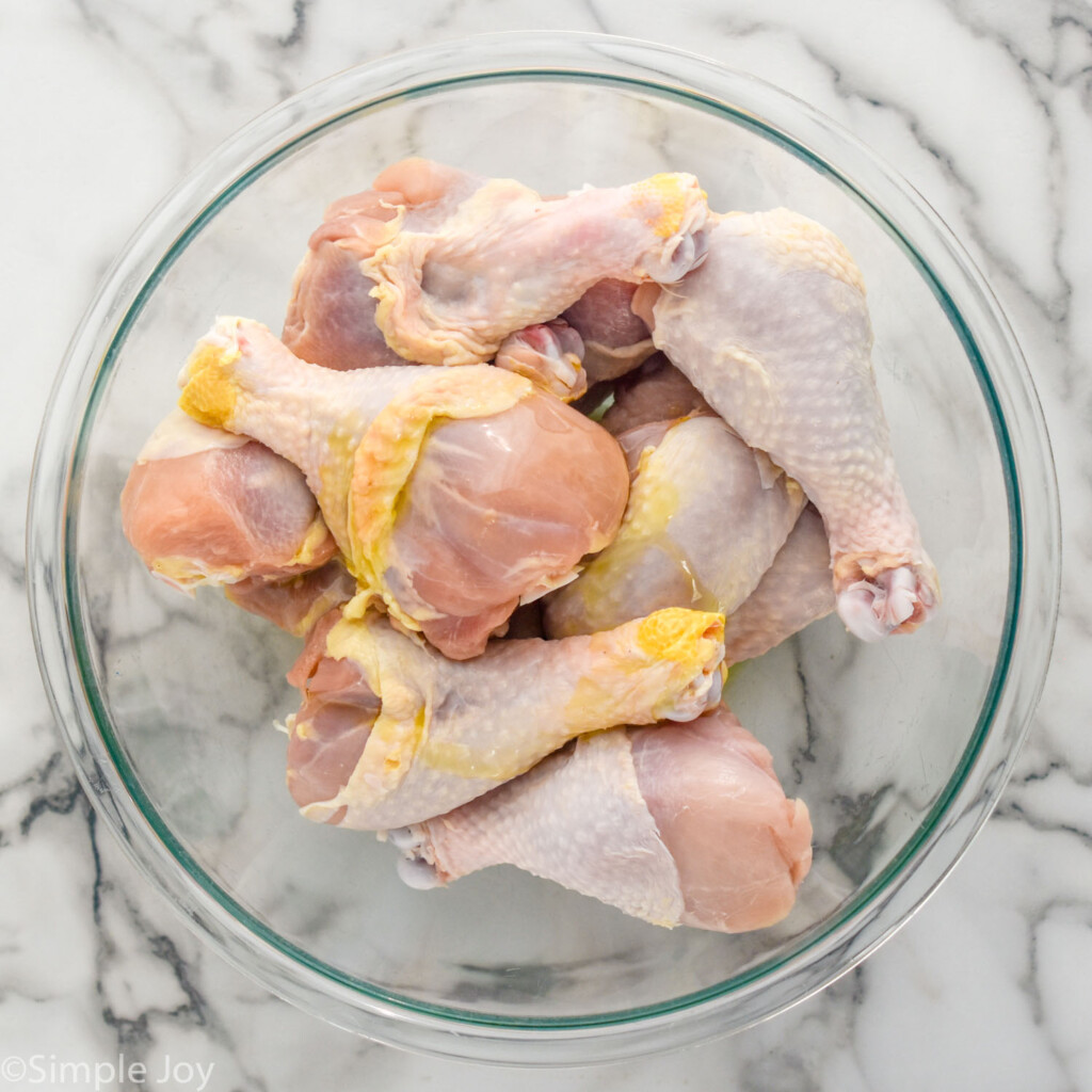 Overhead of glass bowl of chicken legs with olive oil drizzled on top to make Oven Baked Chicken Legs