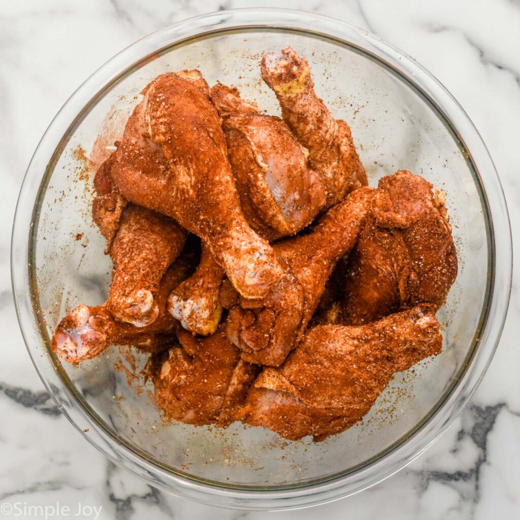 overhead of glass bowl of raw chicken legs with seasonings to make Oven Baked Chicken Legs