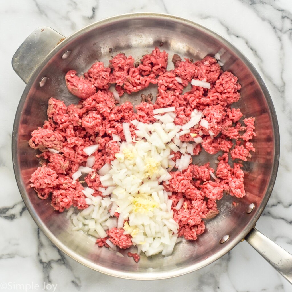 Overhead of stainless steal skillet with ground beef, garlic, and diced onion to make taco meat for Baked Tacos