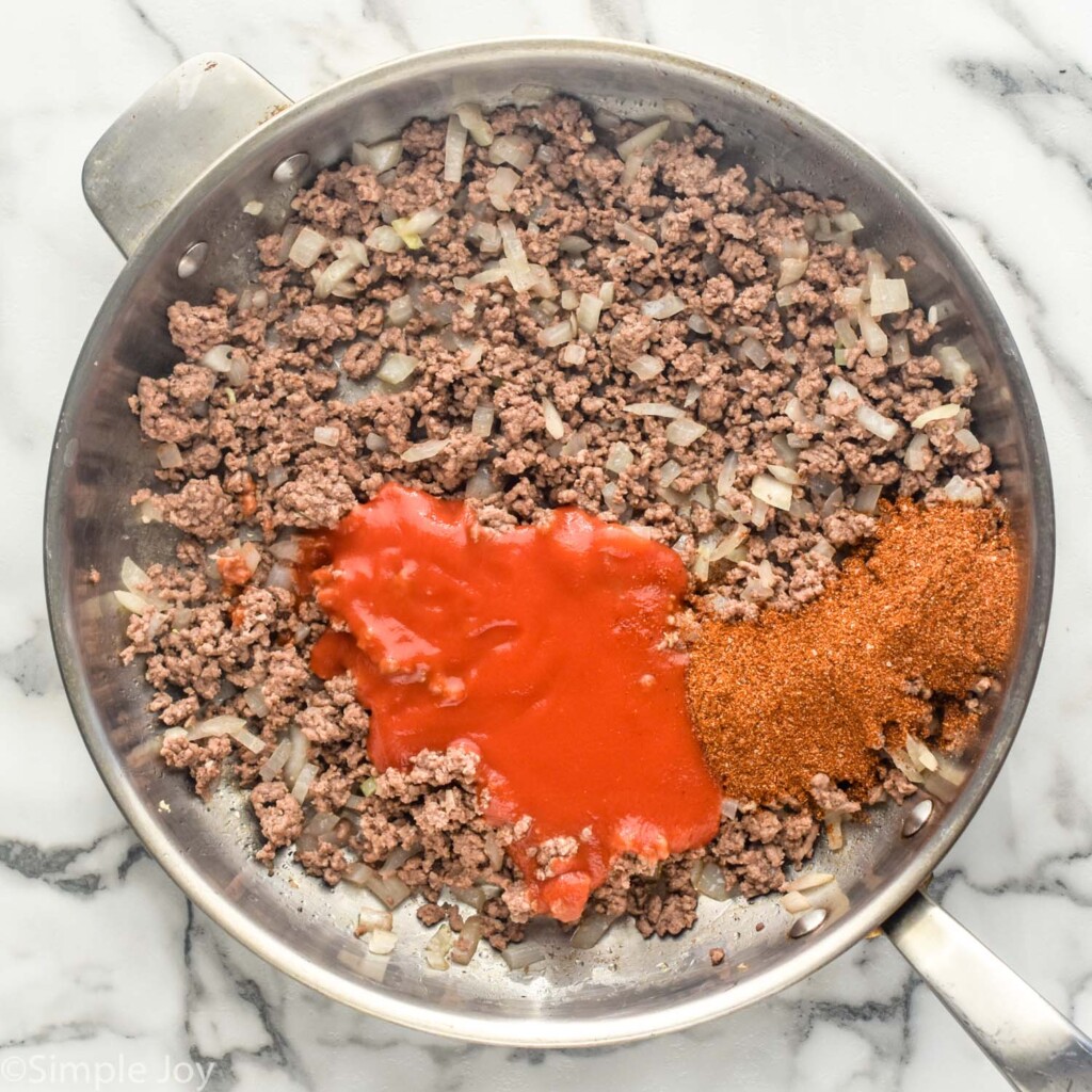 overhead of large skillet of ground beef, garlic, onion, taco seasoning, and tomato sauce to make Baked Tacos