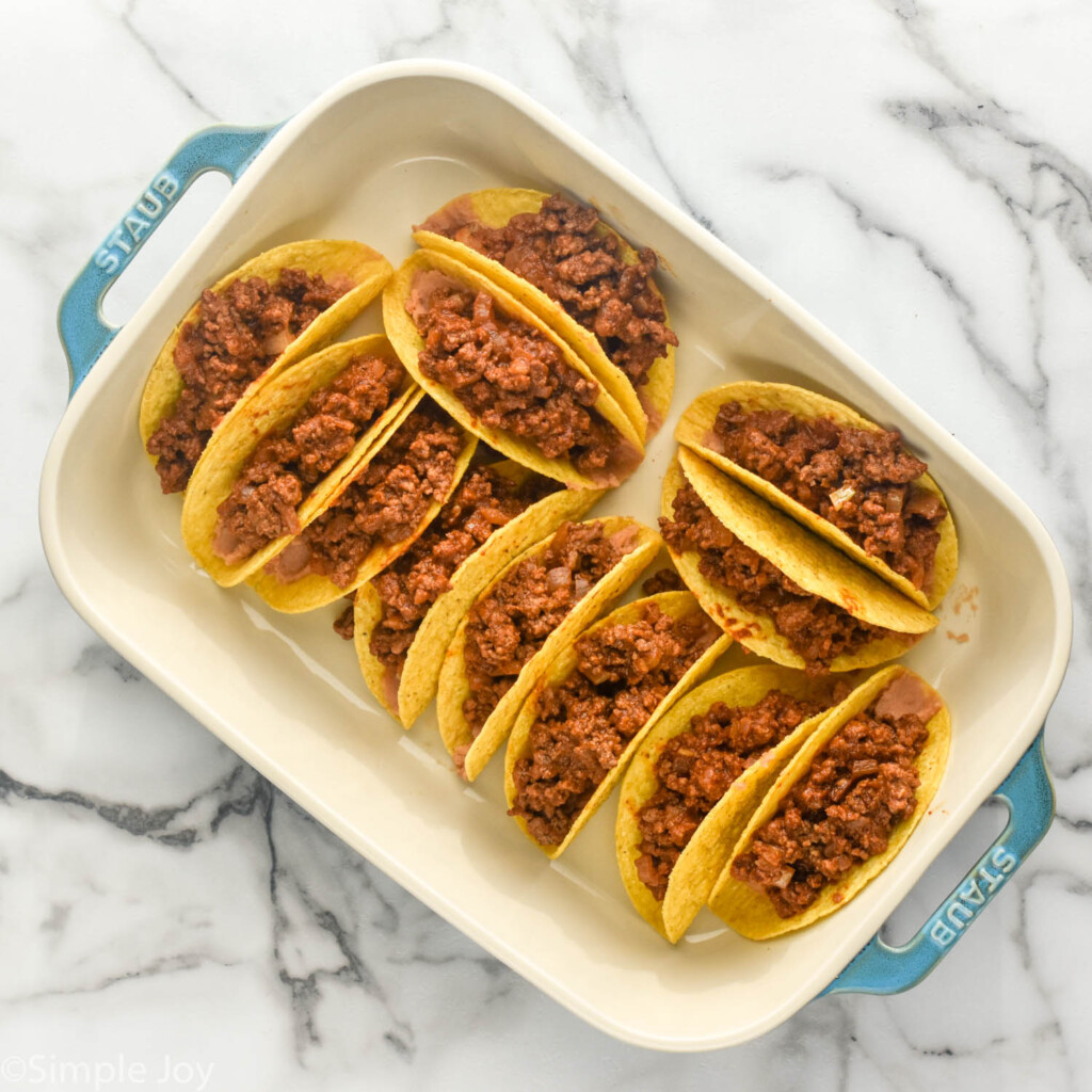 Overhead of casserole dish of hard taco shells with refried beans and taco meat to make Baked Tacos