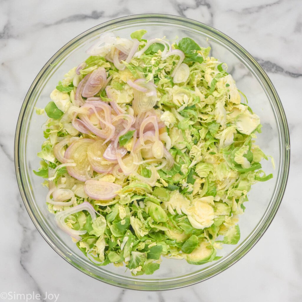 overhead of bowl of shaved brussels sprouts and shallots to make Shaved Brussels Sprout Salad