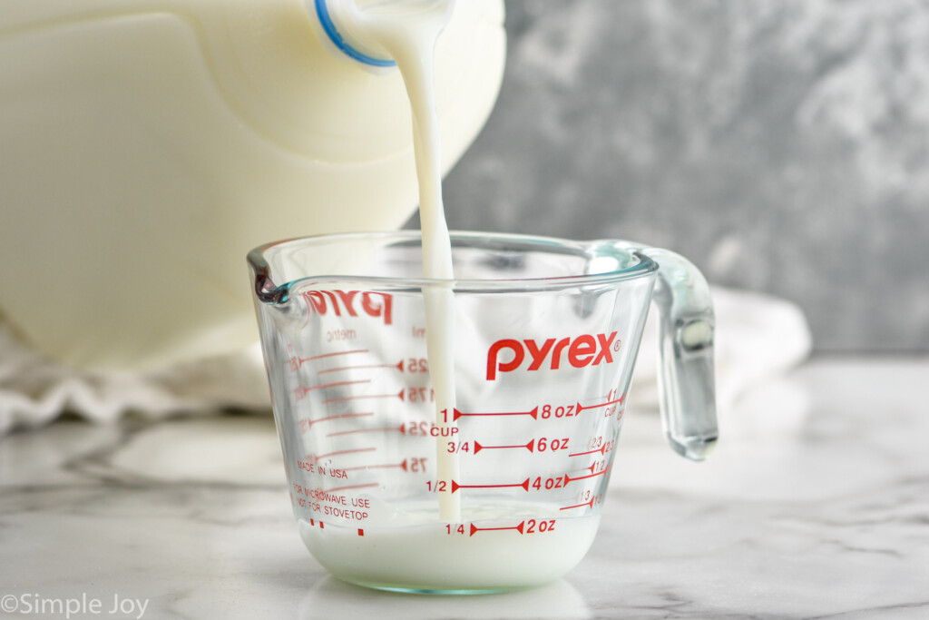 gallon of milk pouring into a glass measuring cup to make Homemade Buttermilk