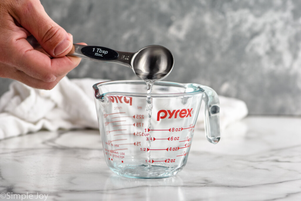 man's hand pouring tablespoon of vinegar into a glass measuring cup to make Homemade Buttermilk