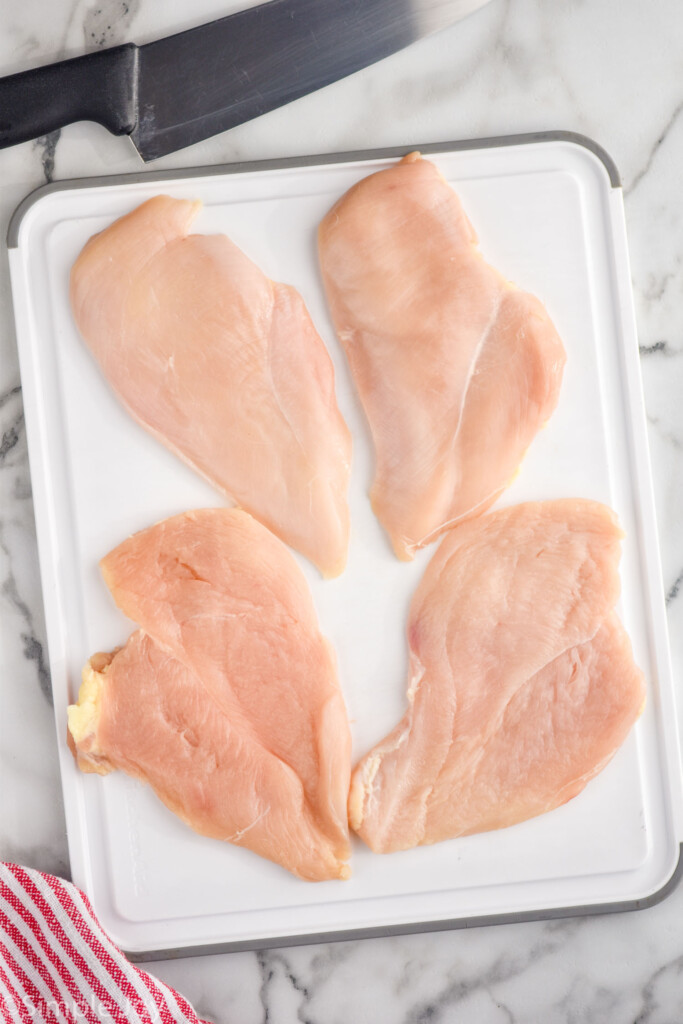 four chicken cutlets on a cutting board with a knife